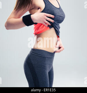 Closeup Portrait einer Fitness-Frau kneifen eine Fett auf ihrem Unterleib auf grauem Hintergrund Stockfoto