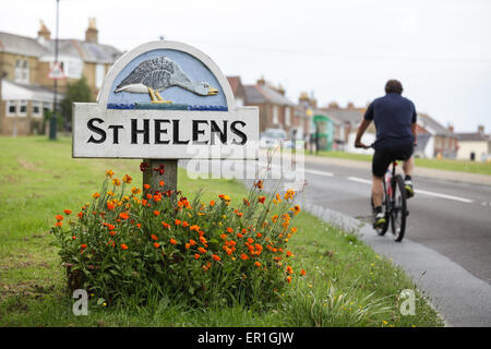 Ein Radsportler, die hinter dem Ortsschild von St. Helens (AKA Goose Island) neben dem Grün auf der Isle Of Wight. Stockfoto