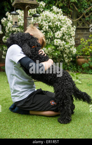 Ein Junge im Garten umarmt seinen Hund Stockfoto