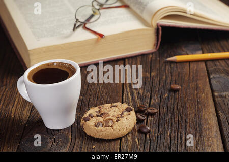 Kaffeetasse mit Schoko-Cookie und altes Buch auf Holztisch Stockfoto