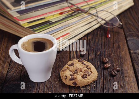 Tasse Kaffee mit Cookie und alten Zeitschriften auf Holztisch Stockfoto