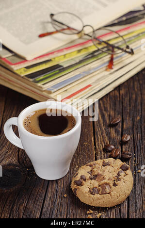 Kaffeetasse mit Schoko-Cookie und alten Zeitschriften auf Holztisch Stockfoto