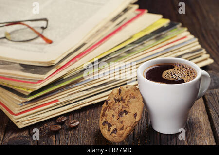 Kaffeetasse mit Cookie und alten Zeitschriften auf Holztisch Stockfoto