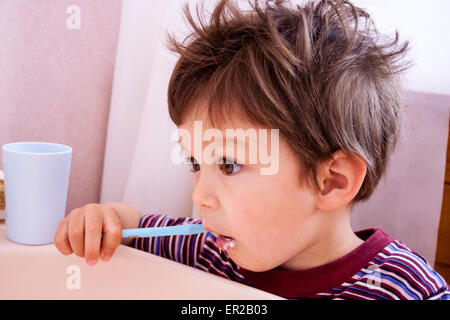 Nahaufnahme von Kopf und Schultern eines kleinen Kindes, Jungen, 3-4 Jahre alt, als er seine Zähne mit blauer Zahnbürste putzt. Die Haare waren zerrümmt, als ich gerade aus dem Bett aufgestanden war. Stockfoto