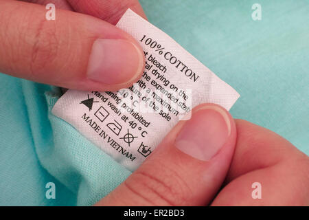 Frauenhand hält Kleidung Label. 100 % Baumwolle. Reinigungsanleitung. Made in Vietnam. Stockfoto