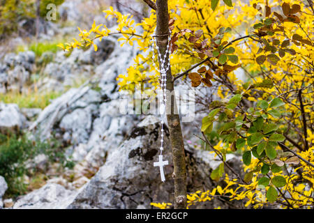 Gebetskette auf einem Baum auf dem Berg Krizevac (Kreuz) in Medjugorje in Bosnien Ed Erzegovina: im Hintergrund bräunlich Bäume, grüne, Unkraut, orange und gelbe Blätter und grauen Felsen Stockfoto