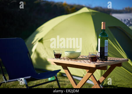 Gläser Wein auf einem Tisch neben dem Stuhl und dem Zelt beim camping Stockfoto