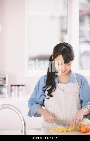 Junge Frau Schneiden von Gemüse in der offenen Küche Stockfoto