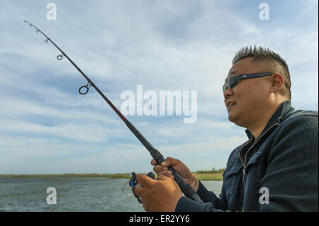 Südlichen Merrick, New York, USA. 24. Mai 2015. Reverend DAVID YI, der Douglaston, Queens, ist Fischen in Merrick Bucht vom Pier von Levy Park & Preserve Memorial Day Wochenende. Der Pastor Gruppe ging in den Park, weil sie nicht zum Jones Beach, Fisch, für die Gegend, die Alleen geschlossen wurden, nach Strand, Kapazität für die Bethpage New York Air Show, gefüllt, die früher aus der Ferne am Himmel hinter ihm zu sehen zu gehen. © Ann Parry/ZUMA Draht/Alamy Live-Nachrichten Stockfoto