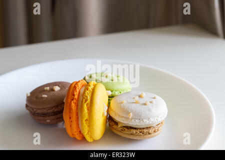 Orange, weiß, braun grüne Makronen auf weißen Teller Stockfoto