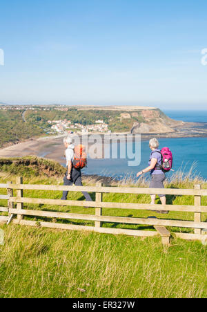 Älteres Paar auf The Cleveland Way coastal Footpath mit Runswick Bay Village in Ferne. North Yorkshire, England, UK Stockfoto