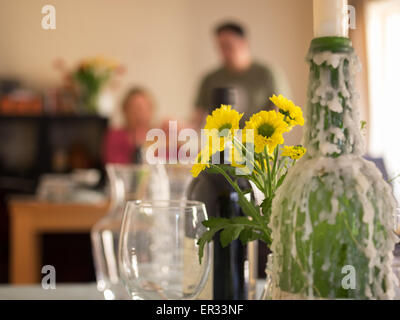 Vorbereitung zum Abendmahl Club Abendessen zu zweit feiern. Kerzenwachs verkrustete Flaschen, Gläser Wein und gelbe Blumen im Vordergrund. Stockfoto