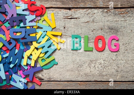 Die bunten Worte "BLOG" mit Holzbuchstaben neben einem Haufen von anderen Buchstaben über alte Holzplatte gemacht. Stockfoto