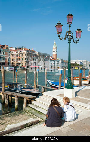 Venedig, Italien - 24. April 2013: Leute sitzen neben dem Canal gegen einen Überblick über klassische venezianische Architektur. Stockfoto