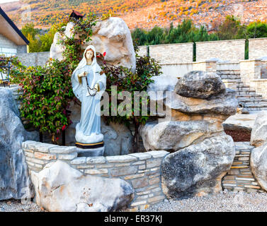 Statue der Jungfrau Maria mit Holz- gebet Perlen Halskette in einem Haus Steingarten mit treesin Medjugorje Stockfoto