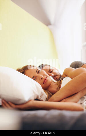 Junges Paar gemeinsam auf Bett liegend. Schöne junge Frau am Bett liegen und Blick in die Kamera mit ihrem Mann schlafen. Stockfoto