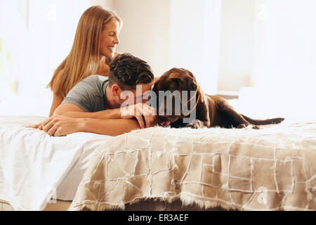 Aufnahme eines jungen Paares entspannen Sie sich auf das Bett mit ihrem Hund. Junger Mann und Frau im Schlafzimmer morgens mit ihrem Hund spielen. Stockfoto