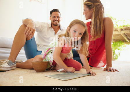 Innenaufnahme der niedliche kleine Mädchen malen mit ihren Eltern sitzen hinter ihr. Familie, sitzen auf dem Fußboden im Wohnzimmer und Kehlenfick Stockfoto