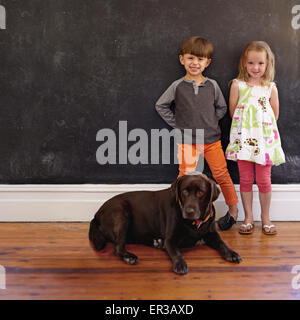 Voller Länge Schuss von lächelnden kleinen Jungen und Mädchen stehen neben Hund zu Hause. Labrador Retriever sitzend im Stock mit Kinder stan Stockfoto