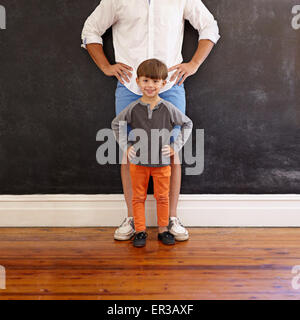 Innenaufnahme von kleinen Jungen und seinem Vater stehen mit ihren Händen auf den Hüften. Little Boy vor Lächeln und seinem Vater ist croppe Stockfoto