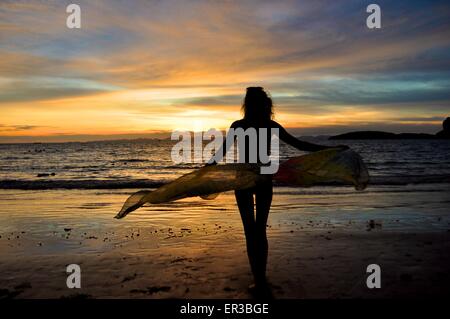 Silhouette einer Frau, die am Strand steht und einen Sarong hält Stockfoto