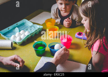 Zwei Kinder färben Ostereier mit ihrem Vater Stockfoto