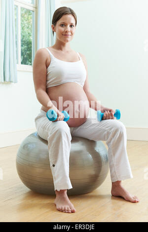 Schwangere Frau sitzen auf einem Gymnastikball mit Gewichten Stockfoto