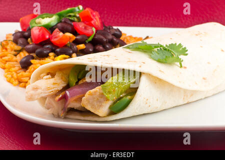 Mexikanisches Huhn Fajita mit grünem Paprika Scheiben und roten Zwiebeln in einer Weizentortilla, mit schwarzen Bohnen und Reis auf der Seite Stockfoto