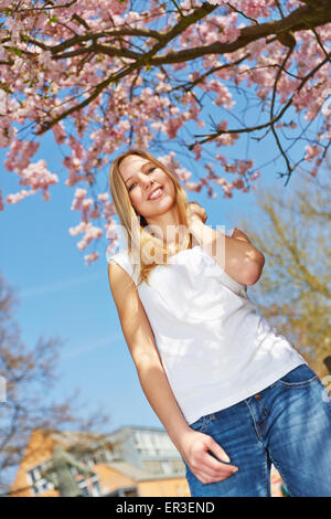 Blonde Mädchen stehen unter einem blühenden Kirschbaum Baum im Frühling Stockfoto