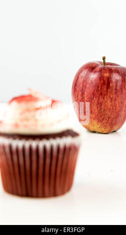 roter Apfel Vs red Velvet Cupcake - Snack Entscheidung zwischen gesunde Ernährung oder Junk-food Stockfoto