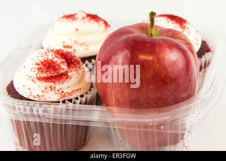 roter Apfel Vs red Velvet Cupcake - Snack Entscheidung zwischen gesunde Ernährung oder Junk-food Stockfoto