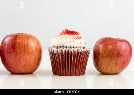 roter Apfel Vs red Velvet Cupcake - Snack Entscheidung zwischen gesunde Ernährung oder Junk-food Stockfoto