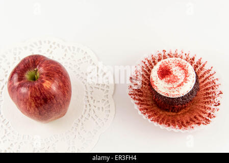 roter Apfel Vs red Velvet Cupcake - Snack Entscheidung zwischen gesunde Ernährung oder Junk-food Stockfoto