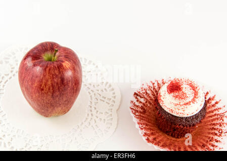 roter Apfel Vs red Velvet Cupcake - Snack Entscheidung zwischen gesunde Ernährung oder Junk-food Stockfoto