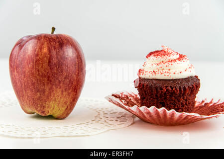 roter Apfel Vs red Velvet Cupcake - Snack Entscheidung zwischen gesunde Ernährung oder Junk-food Stockfoto