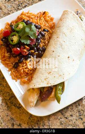 Mexikanisches Huhn Fajita mit grünem Paprika Scheiben und roten Zwiebeln in einer Weizentortilla, mit schwarzen Bohnen und Reis auf der Seite Stockfoto