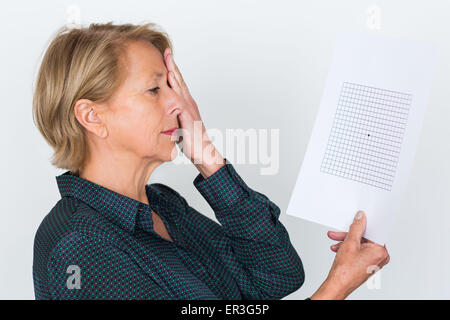 Ältere Frau betrachten ein Amsler-Gitters, Makula-Degeneration zu erkennen. Stockfoto