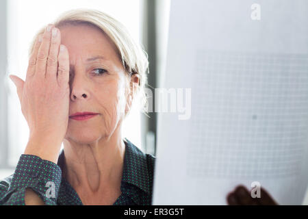 Ältere Frau betrachten ein Amsler-Gitters, Makula-Degeneration zu erkennen. Stockfoto