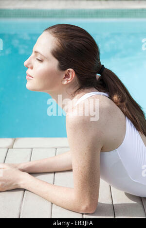 Junge Frau mit geschlossenen Augen neben Pool Sonnenbaden Stockfoto