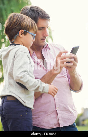 Vater und seinem kleinen Sohn betrachten Smartphone zusammen im freien Stockfoto