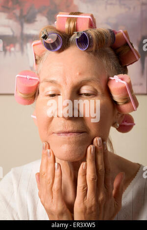 Dame mittleren Alters in Lockenwickler beim Schminken Stockfoto