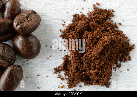 Gemahlenen Kaffee in einem Löffel und Kaffeebohnen auf weißem Holz Hintergrund Stockfoto
