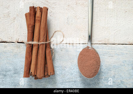 Einige Zimtstangen mit einem natürlichen Seil gebunden. Als nächstes ein Löffel mit einigen Puderzucker Zimt. Alle auf einem weißen Holztisch. Ansicht von oben Stockfoto