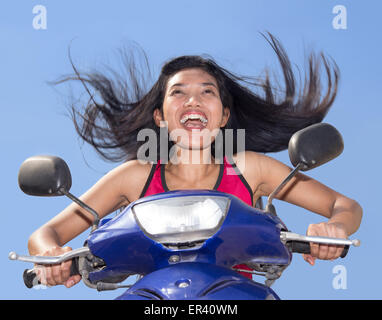 Frau mit fliegenden Haare auf einem Motorrad auf einem blauen Hintergrund Stockfoto