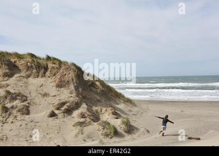 Eine Frau mit ausgestreckten an einem Strand in der Nähe von Dünen laufen. Stockfoto