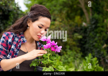 junge Frau riechen eine Blume im Garten Stockfoto