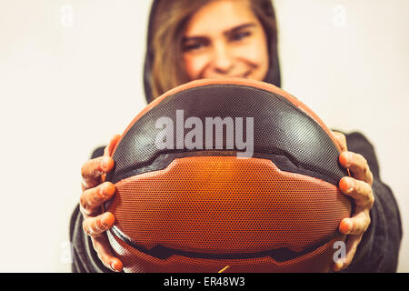 Mädchen hält einen Basketball und lächelnd. Sie trägt einen Sport Hoodie. Schöne, warme Farben des Fotos. Stockfoto