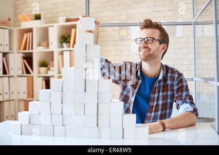 Glücklich Architekt in Casualwear Bau Papier Pyramide im Büro Stockfoto