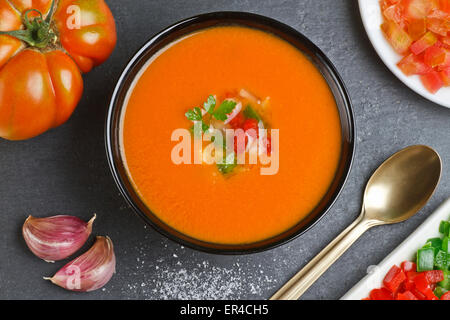 Spanische Gazpacho, goldenen Löffel, Tomaten, Paprika und Knoblauch auf einem Schiefer Teller Stockfoto