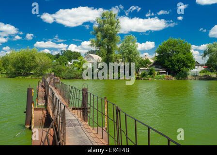 Alten Ponton-Fußgängerbrücke über grüne Flüsschen im ukrainischen Dorf. Stockfoto